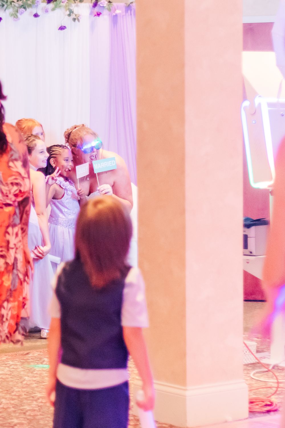 Wedding reception guests having fun with props in front of a purple and white backdrop.