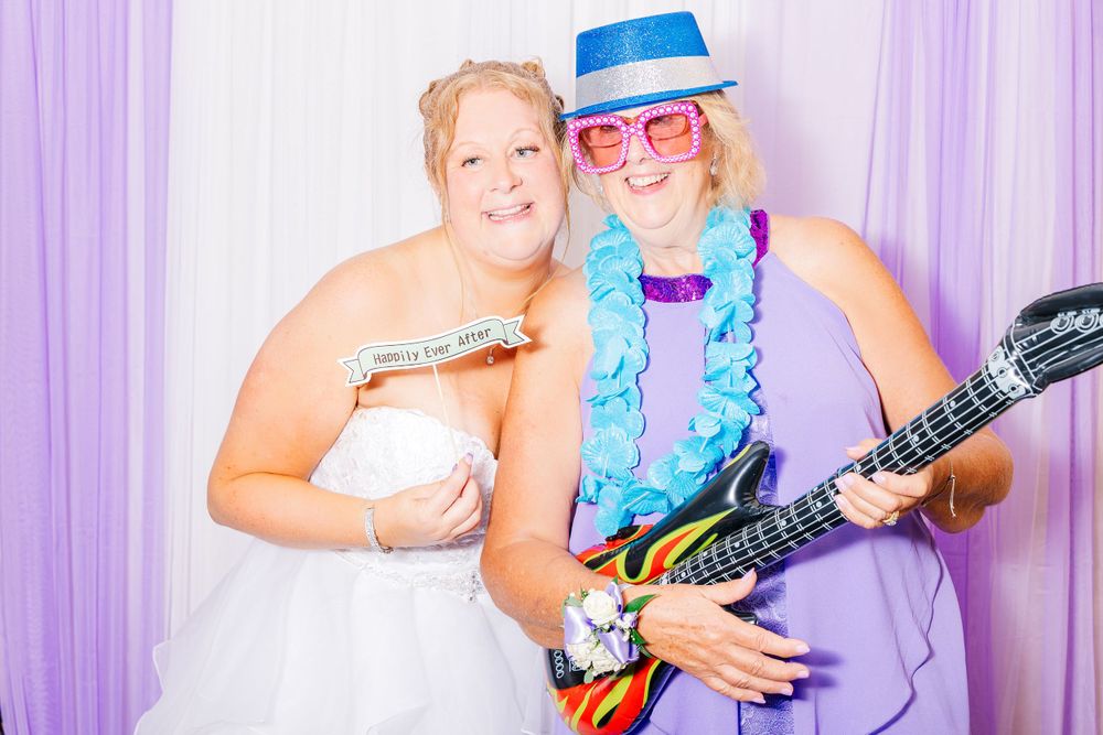 Wedding photo booth scene with guests posing with a toy guitar and fun accessories.