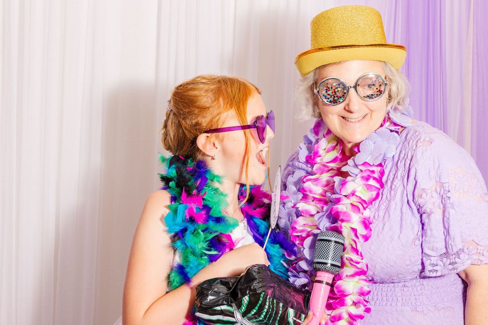 Two attendees having fun in a photo booth with colorful leis and party props.