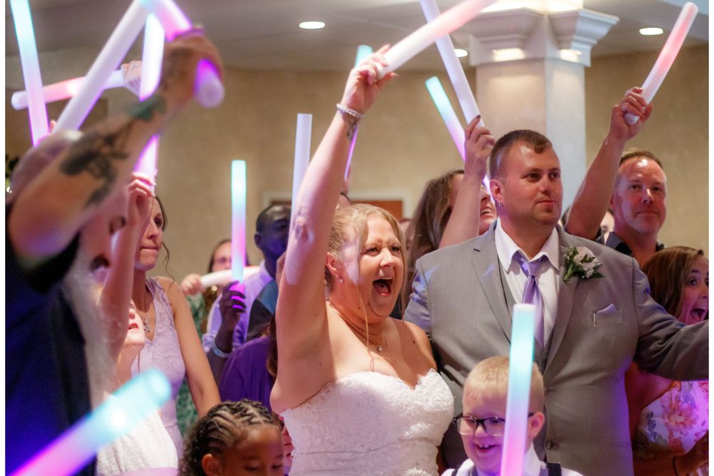 Wedding party celebrates with glowing foam sticks during an indoor reception.