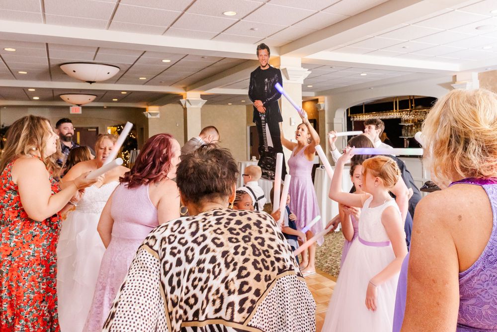 Wedding guests dance and celebrate on a dance floor decorated with purple lighting.