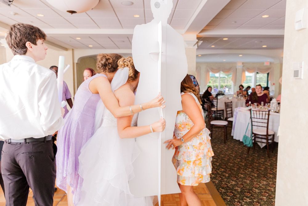 Wedding guests dance and hide playfully behind a column at an indoor reception venue.