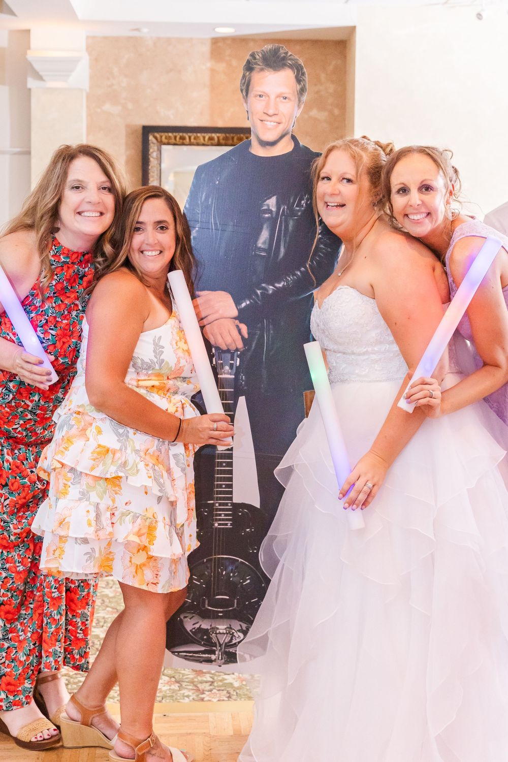 Group poses with glow sticks next to a cardboard cutout at a wedding reception.