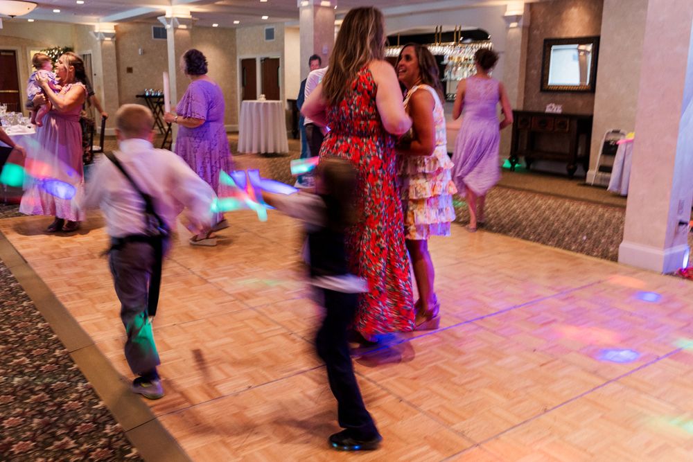 Wedding guests dancing on a carpeted dance floor with purple mood lighting.