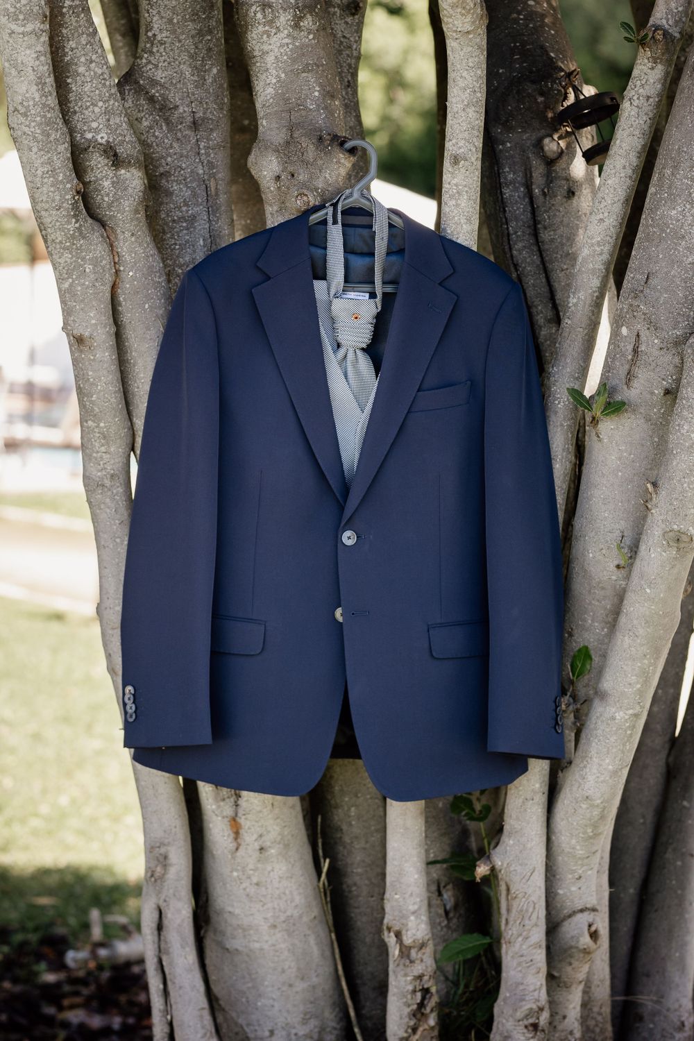 Navy blue suit jacket hanging on tree branches for wedding day photography.