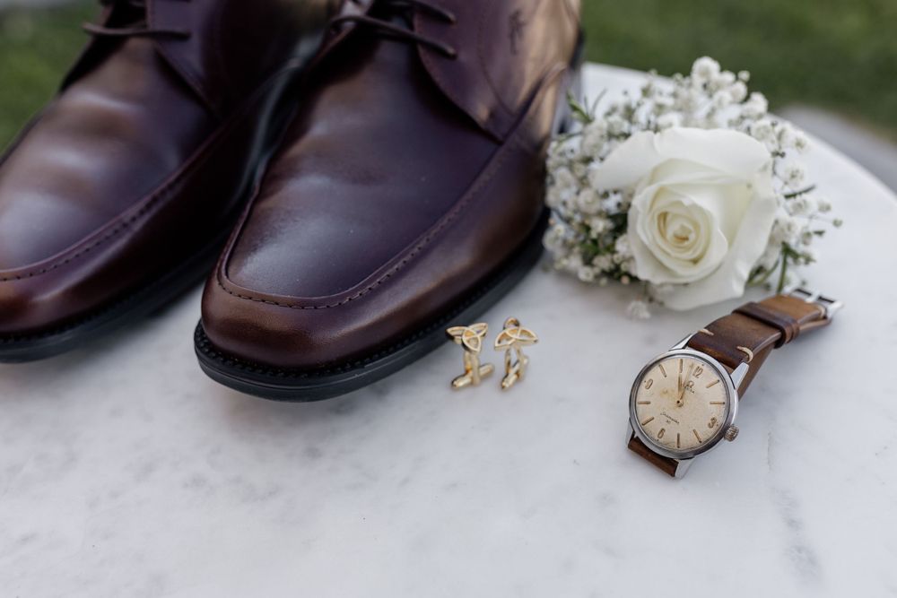 Brown leather dress shoes with wedding accessories including watch and white rose boutonniere.
