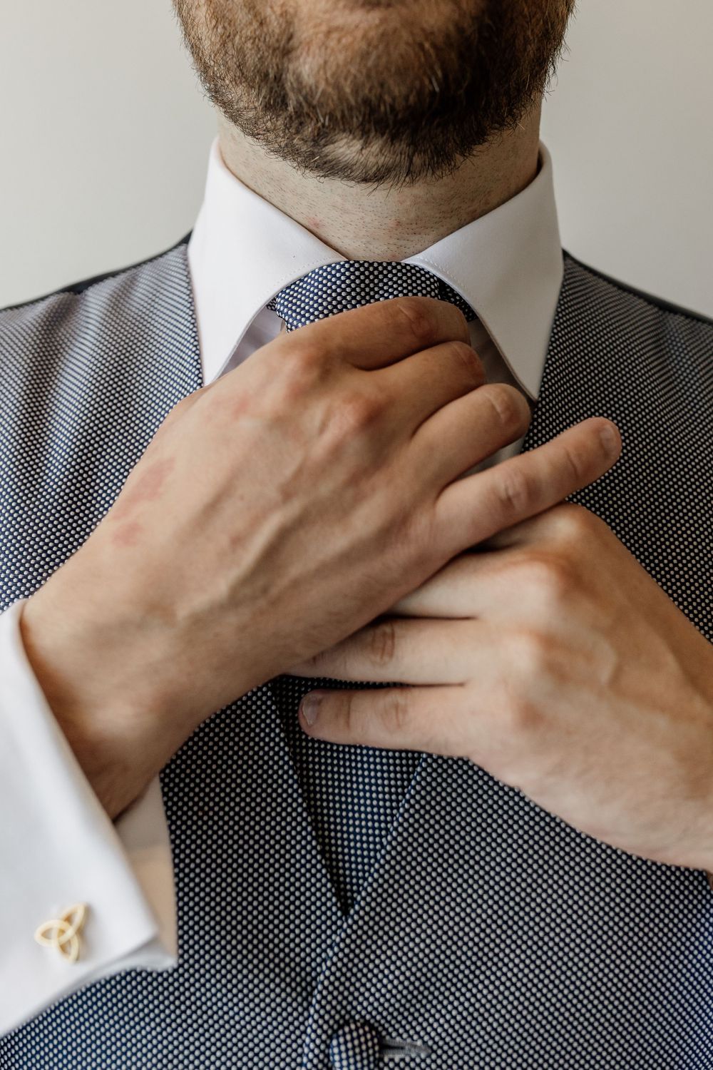 Close-up of hands adjusting a patterned tie and formal suit collar.