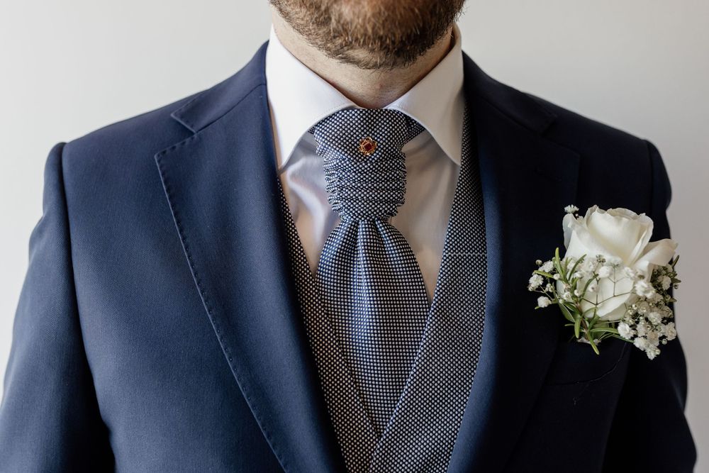 Navy suit jacket with gray vest, patterned tie, and white boutonniere for formal wedding attire.