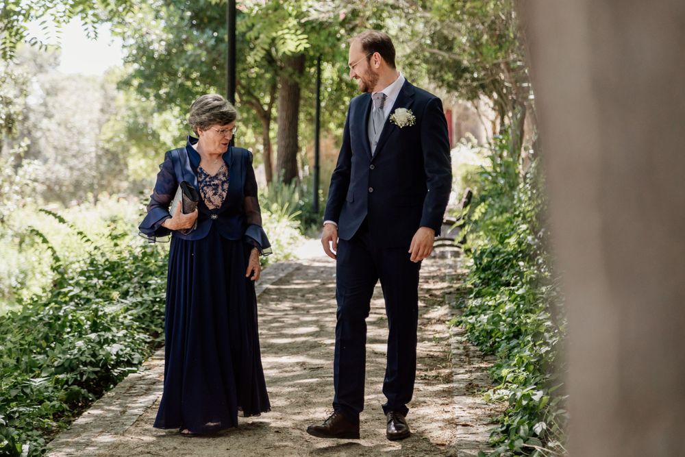 Wedding guests share a moment while walking along garden pathway.