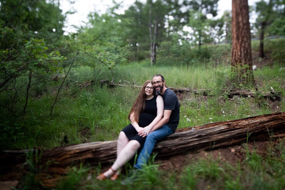 A couple sits together on a fallen log in a serene forest setting.