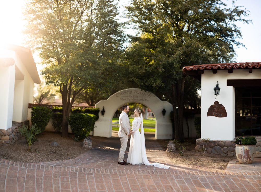 Wedding couple poses beneath Spanish-style archway during golden hour.