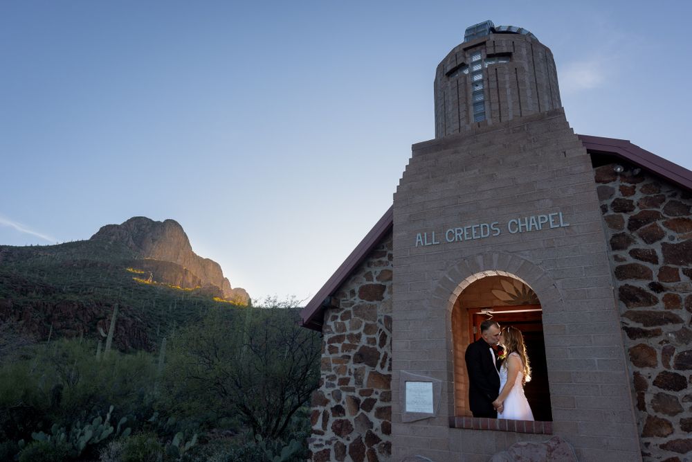A chapel entrance framed by mountains and desert landscape at dusk.