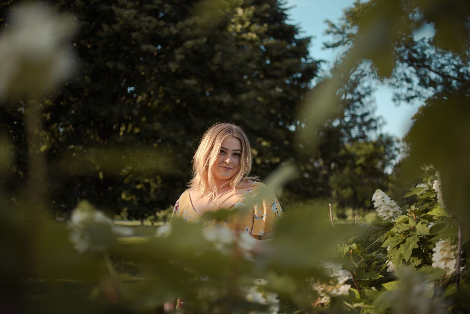 Soft portrait through foliage with sunlit bokeh effects in a garden setting.