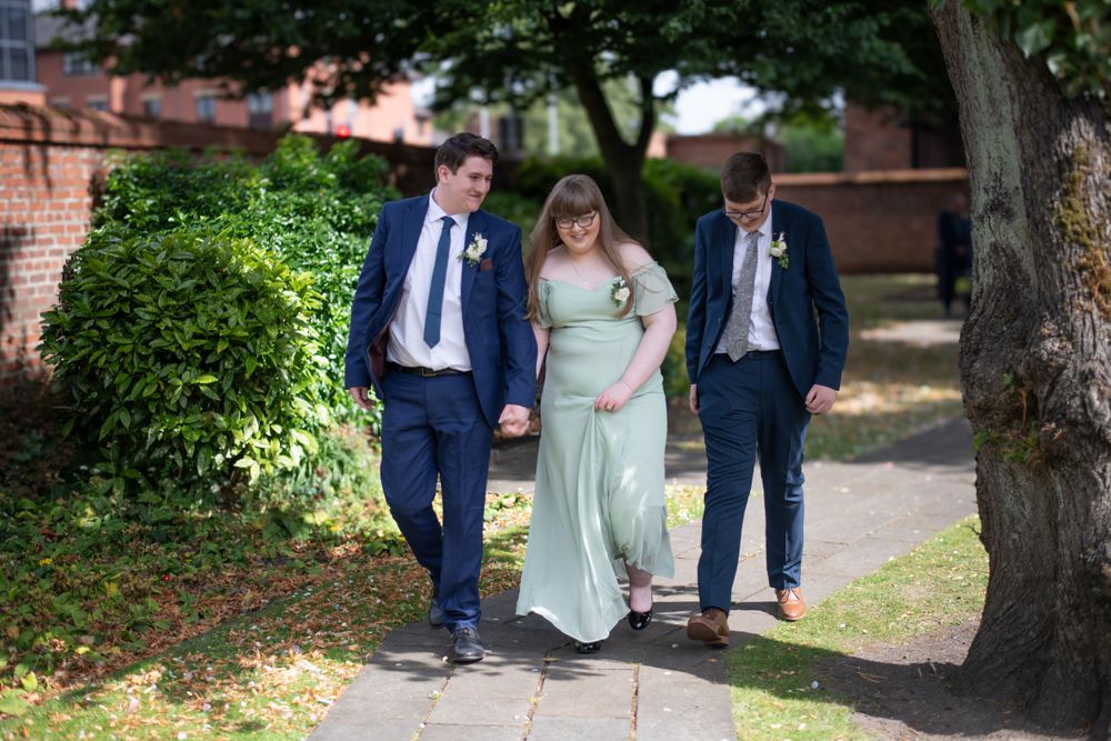 Wedding party walks together on garden path in formal attire.