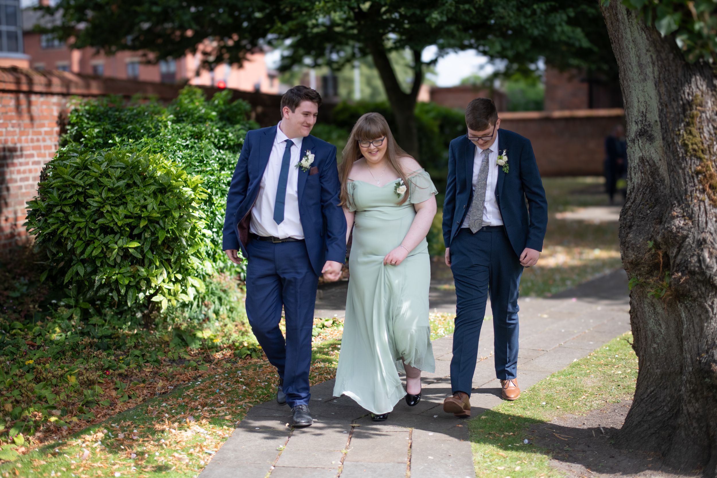 Wedding party walks together on garden path in formal attire.