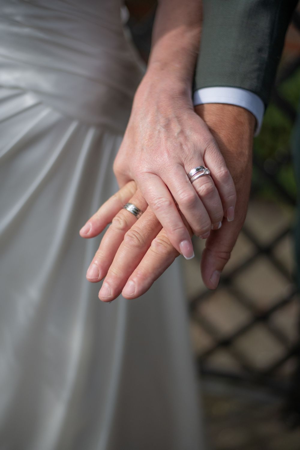 Close-up of newlyweds' hands showing wedding rings against white dress.