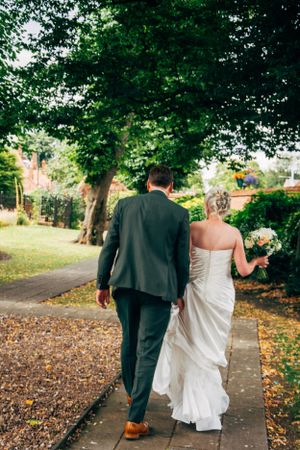 A couple walking along a tree-lined path in wedding attire on their special day.