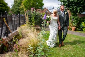 A couple strolling through a garden path surrounded by lush greenery and flowers.