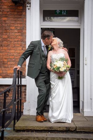 A couple posing on brick building steps in formal wedding attire.