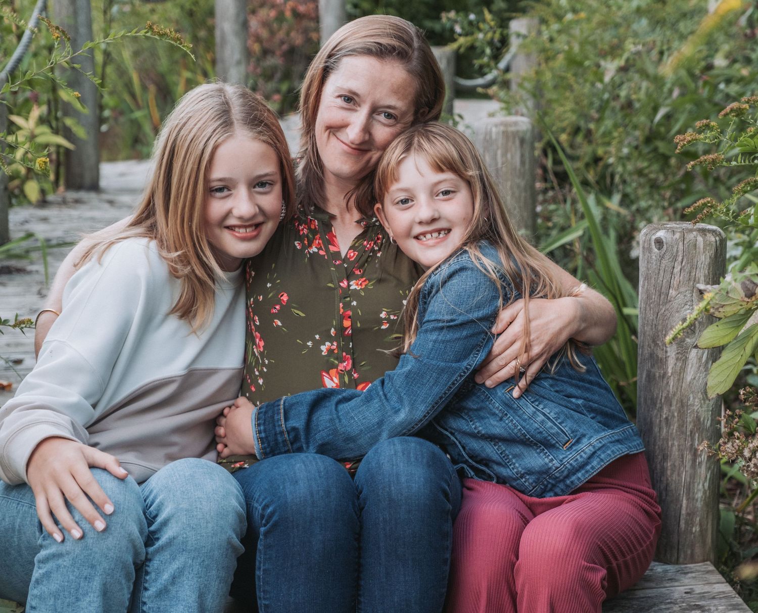 A happy family sitting together on outdoor wooden steps surrounded by greenery on a sunny day. Taken at Fort Williams in Cape Elizabeth, ME