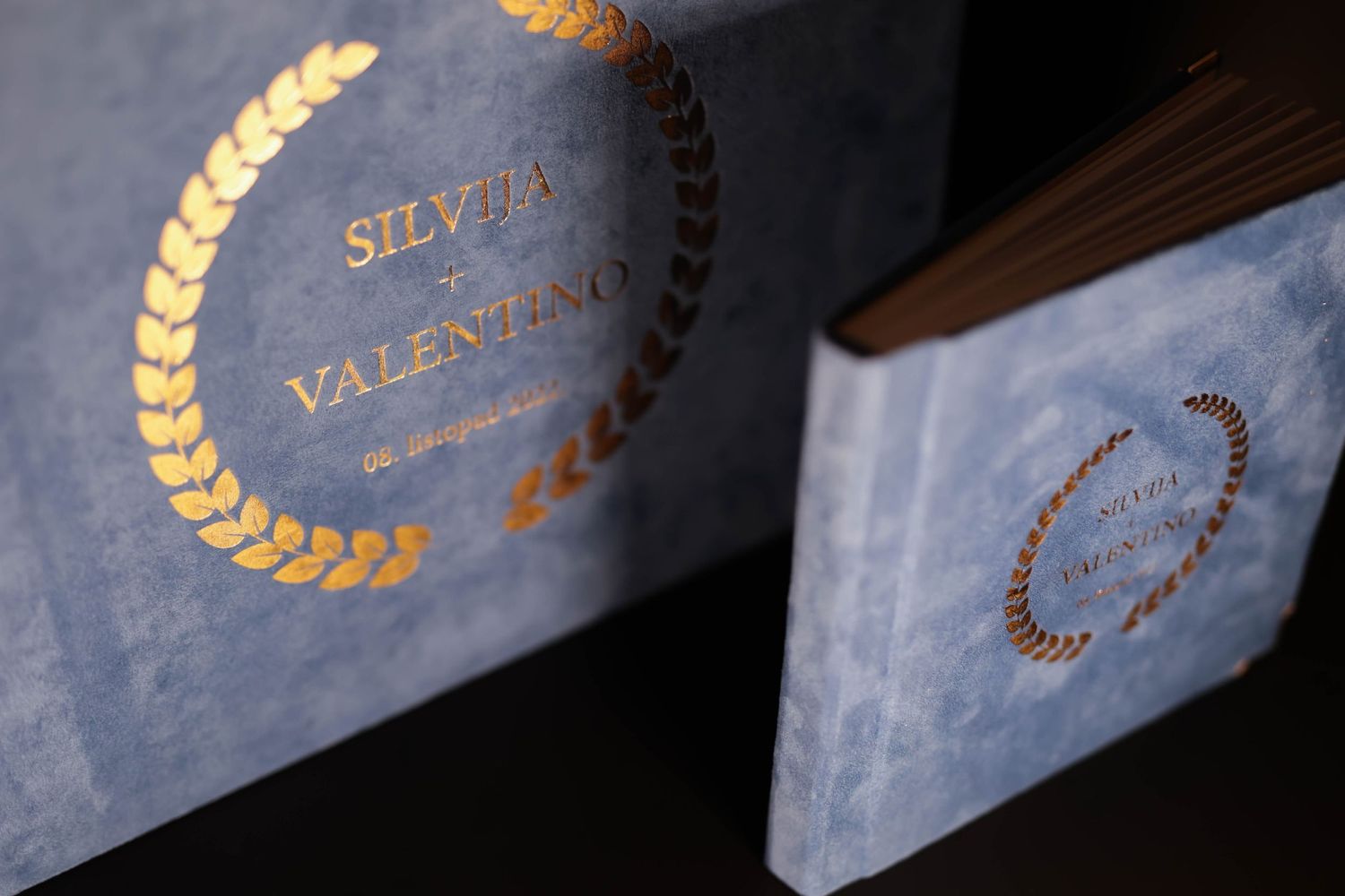 Close-up of blue wedding albums with gold foil lettering and laurel wreath designs.