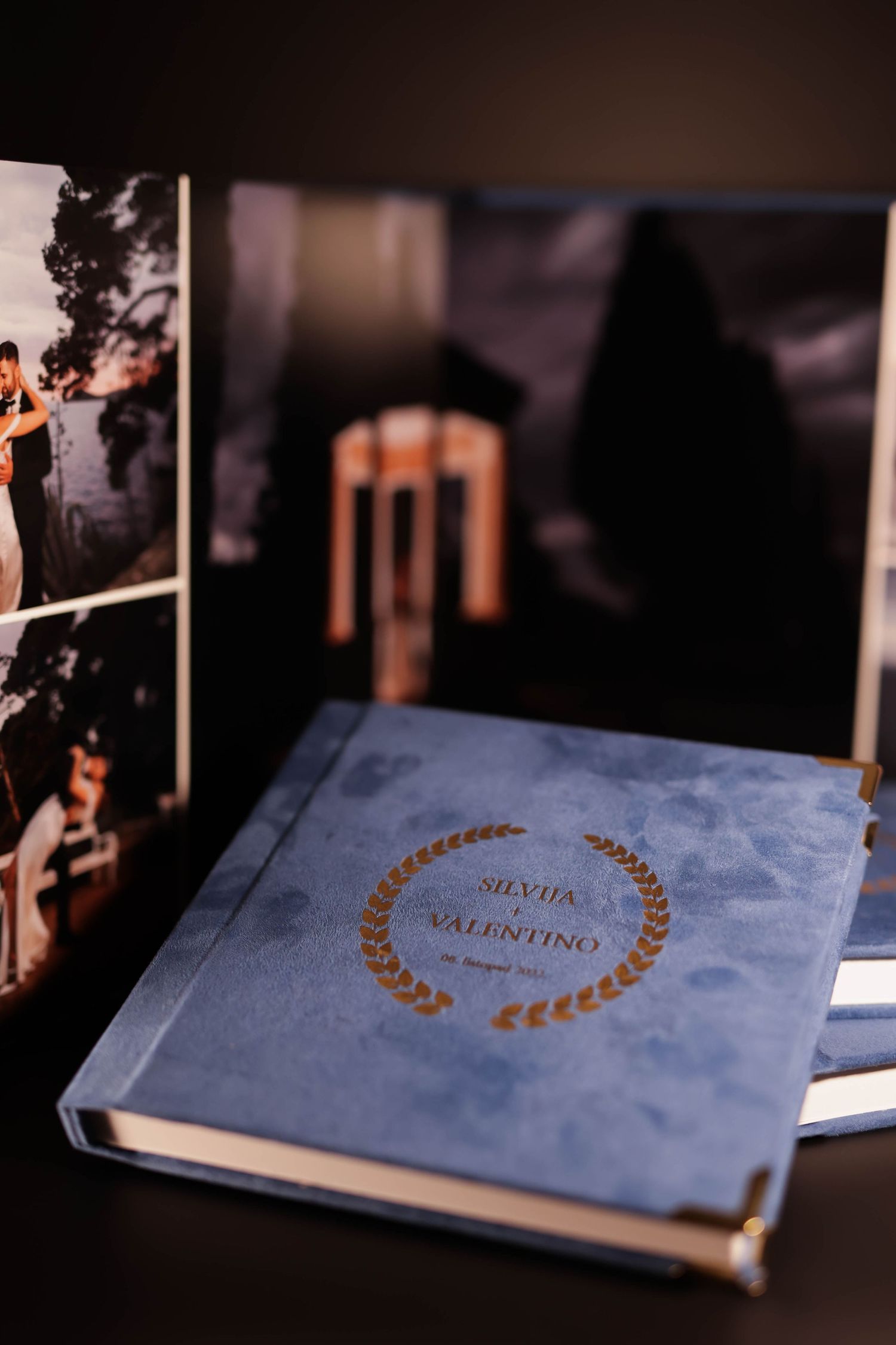 Blue wedding album with gold embossing displayed against a backdrop of romantic photographs.