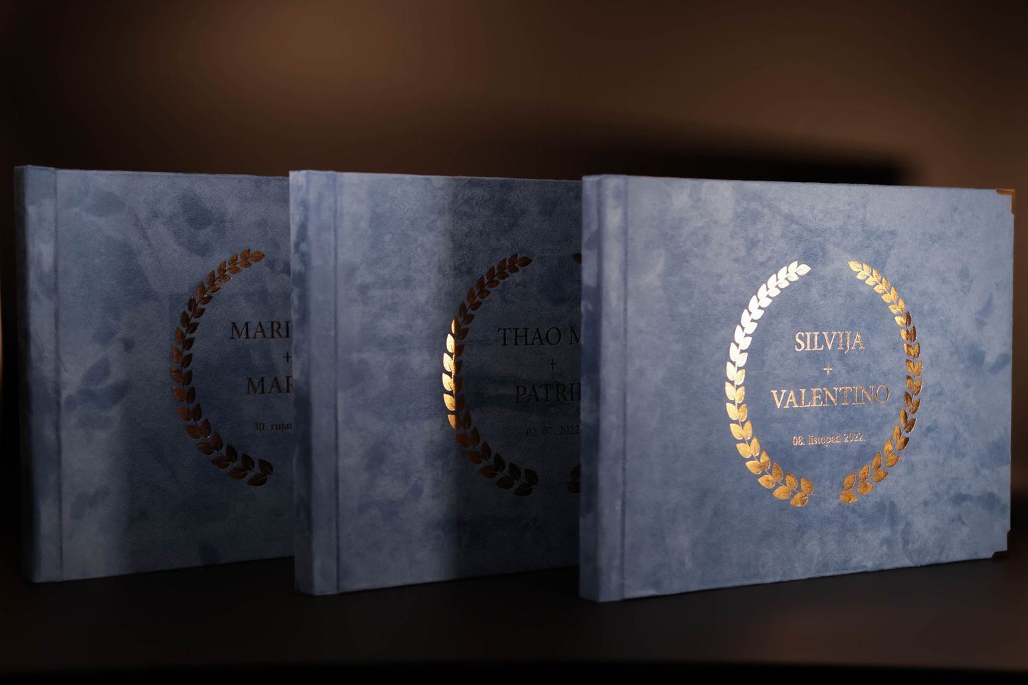 Three elegant blue wedding albums with gold foil wreath designs.