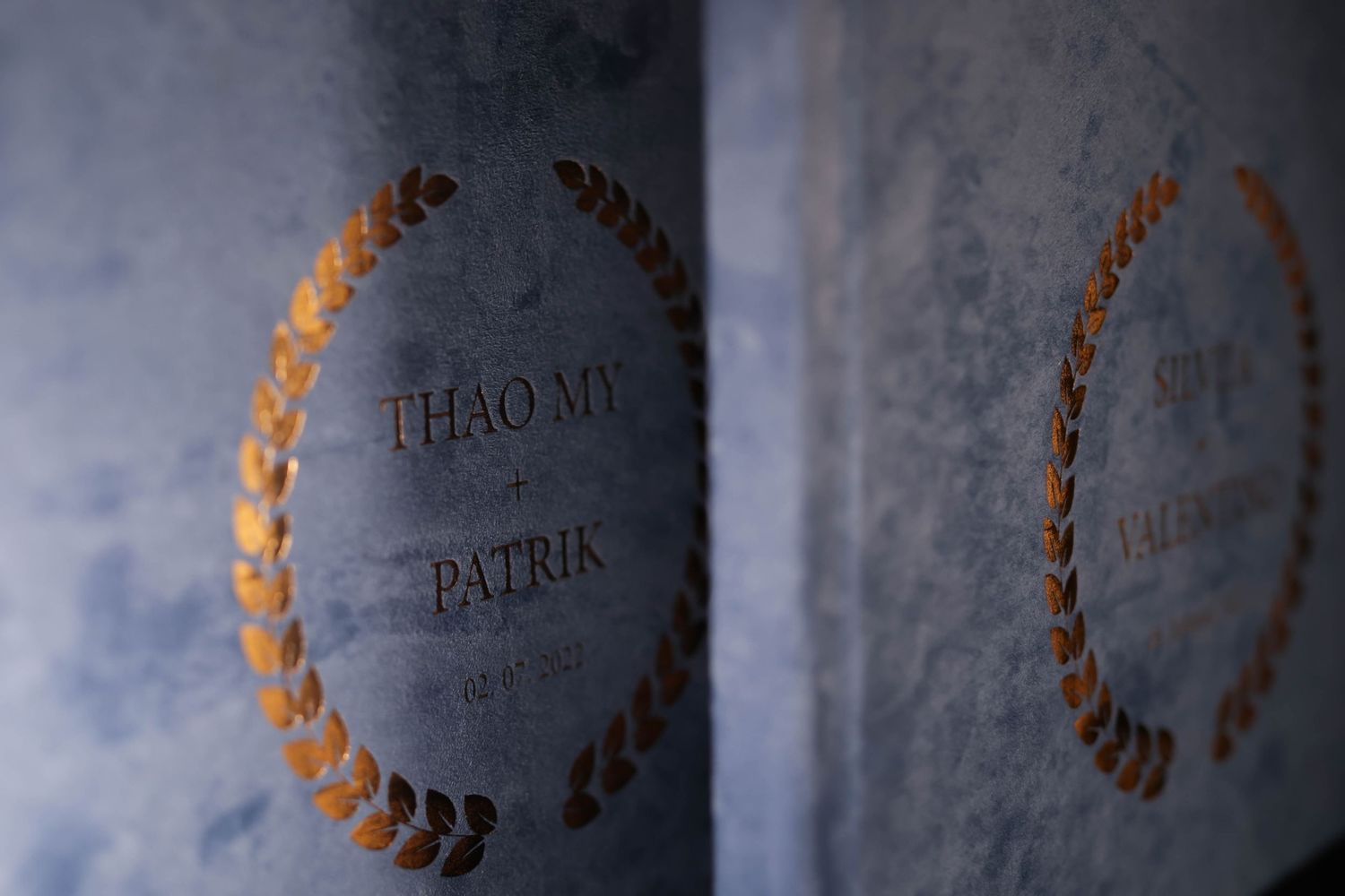 Close-up of wedding album cover with gold foil text and decorative wreath design.