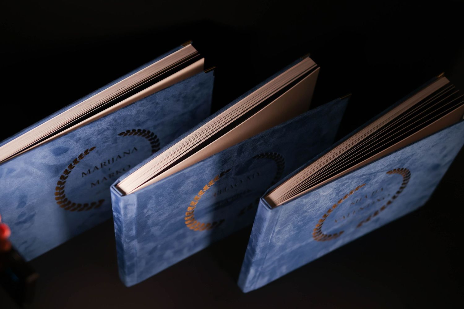 Three blue wedding albums displayed at an angle showing gold embossed details on their covers.