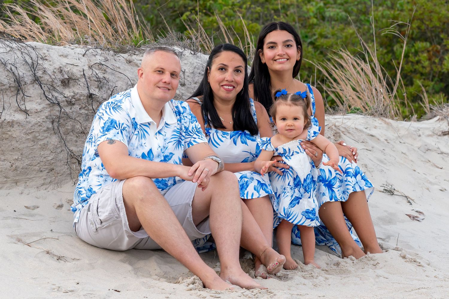 A group wearing matching blue and white floral outfits sits together on a sandy beach.