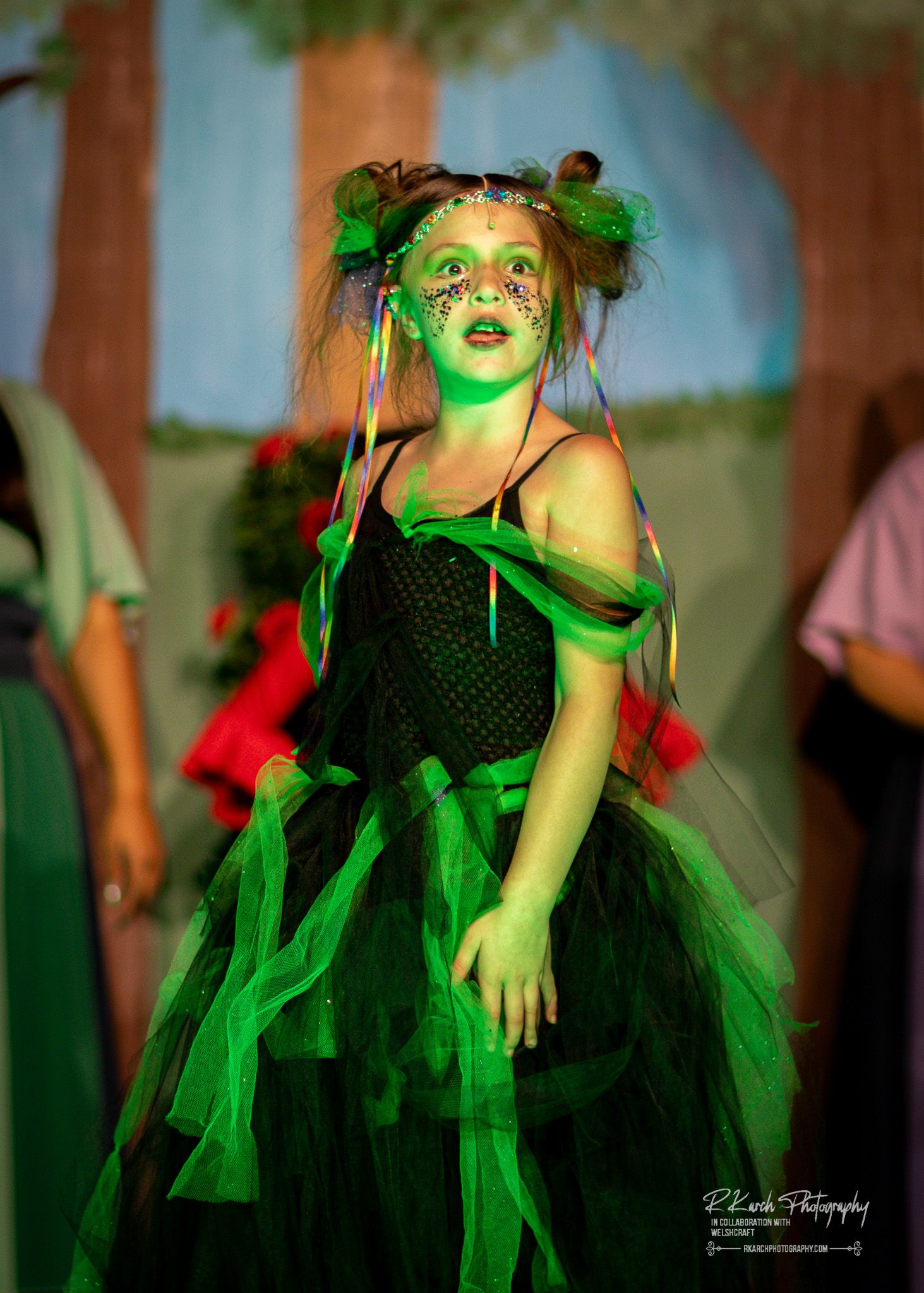 A collection of five photos shows a child in a black and green fairy costume twirling and posing in soft indoor lighting.