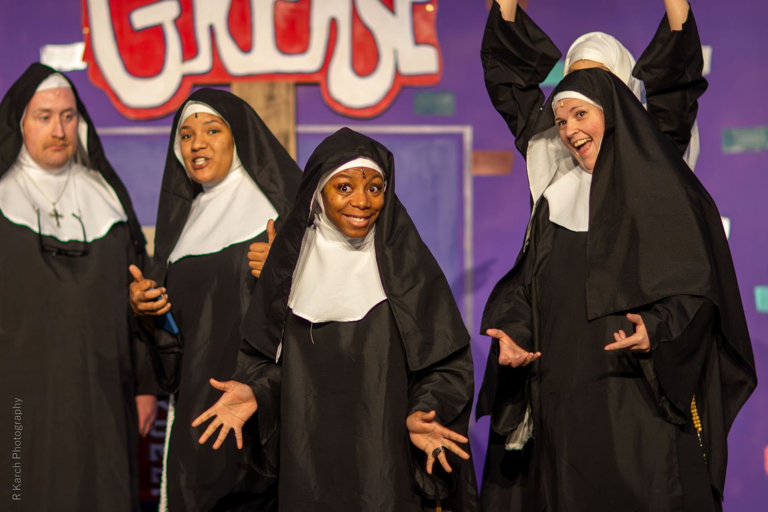 Performers in black and white nun costumes sing and gesture expressively on stage during a theatrical production.