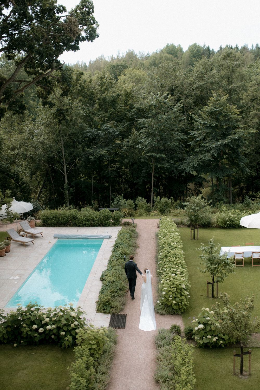 A wedding portrait with serene outdoor swimming pool surrounded by lush greenery and garden paths creates an elegant wedding venue setting.