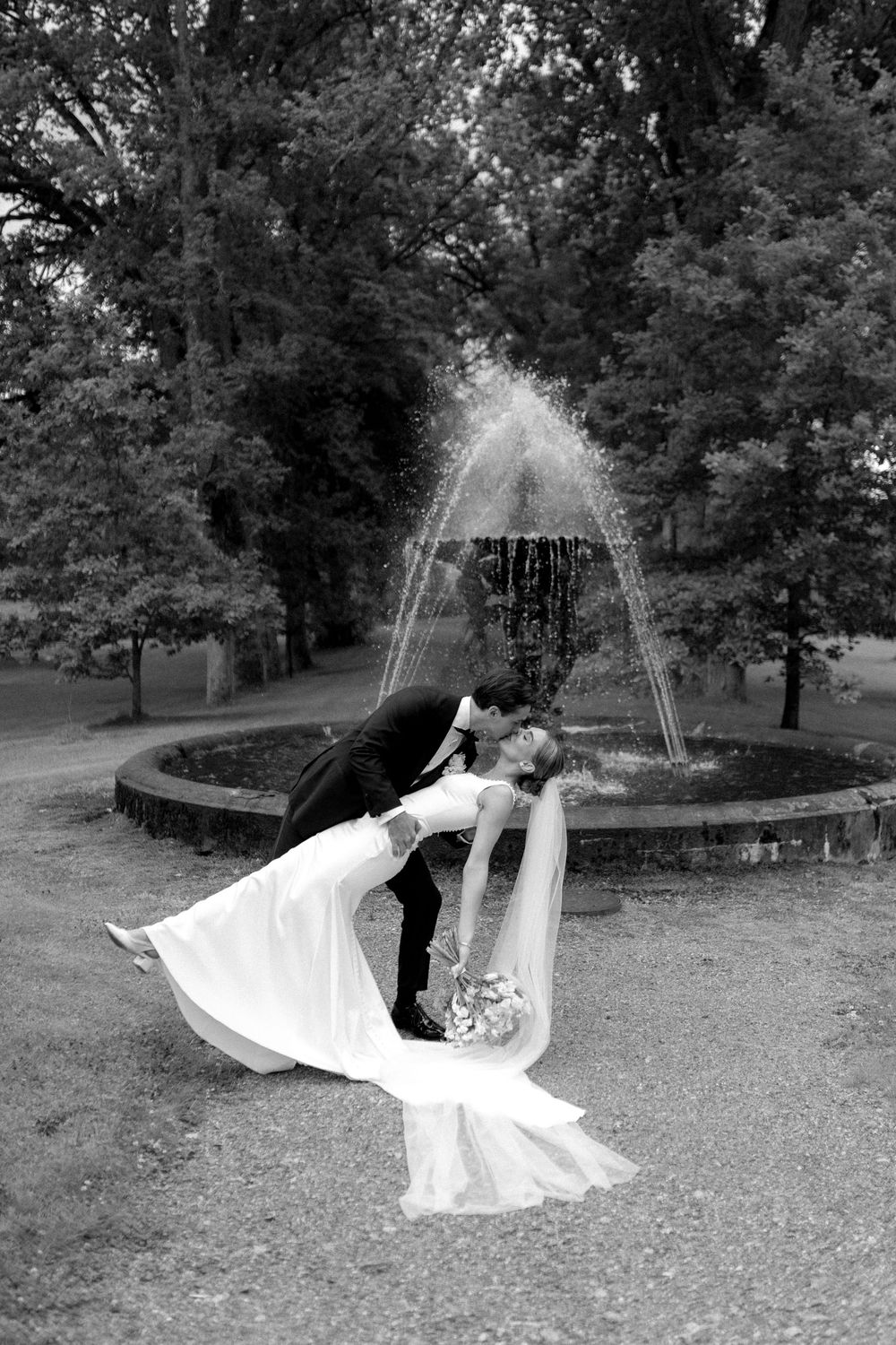 A  romantic black and white wedding portrait of a couple kissing in front of a fountain in a garden in Fagervik, Finland.