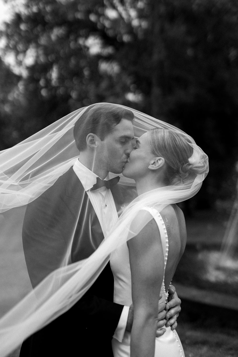 A romantic black and white wedding portrait showing a couple in wedding attire kissing as a veil flows in the breeze in Fagervik, Finland.