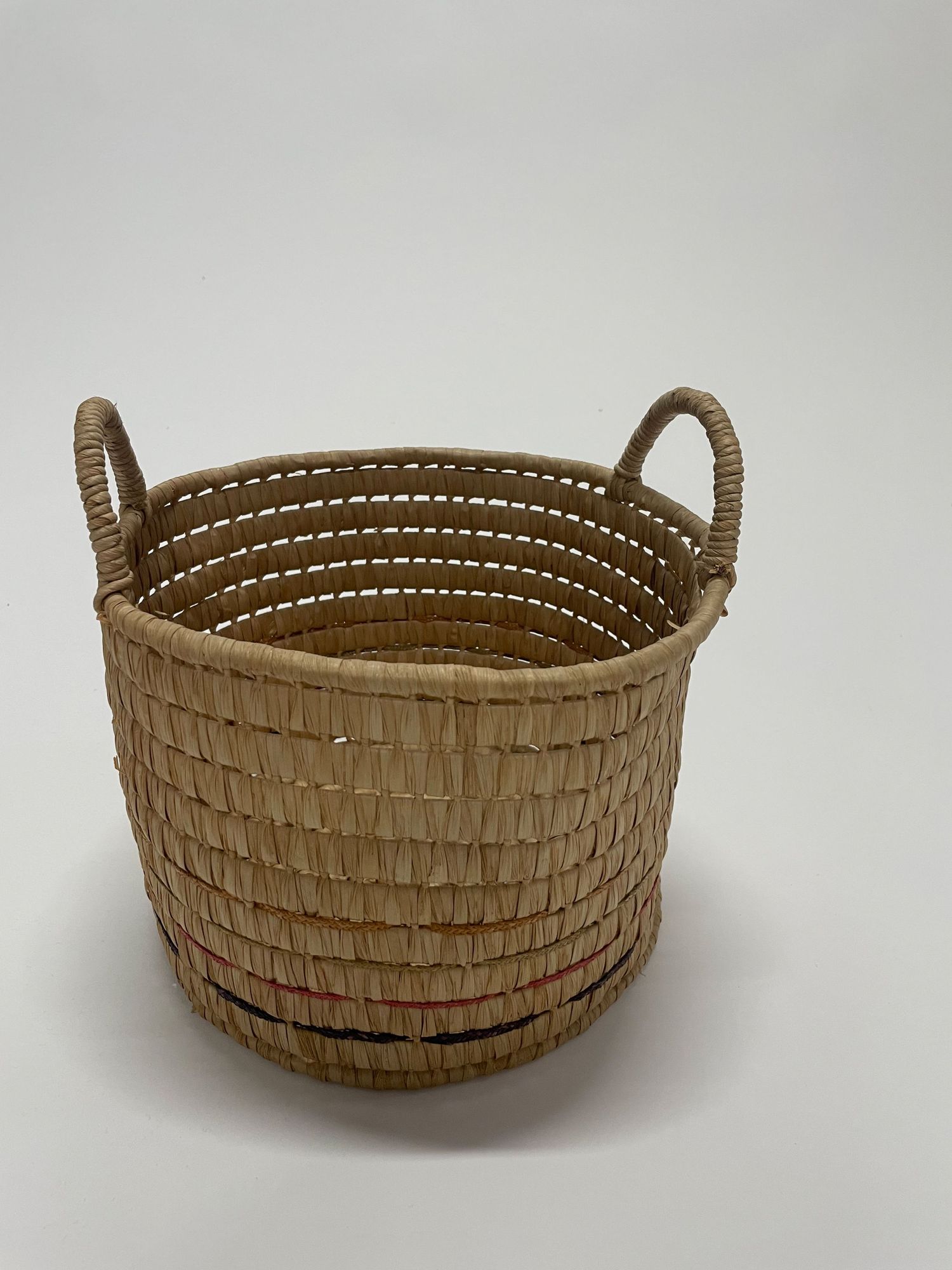 A round woven basket with handles made from natural straw materials.