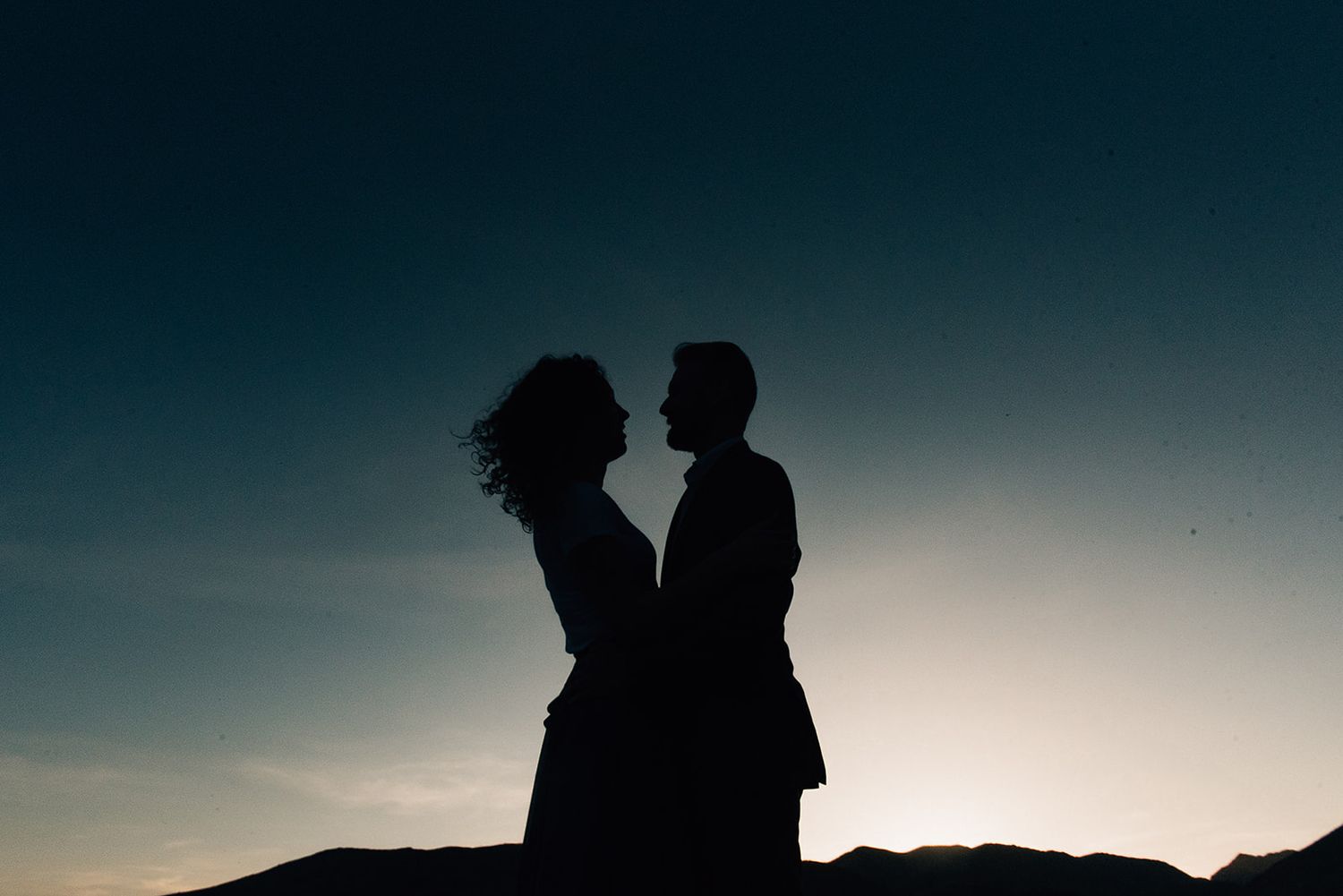 Silhouette of couple embracing against sunset sky on hilltop.