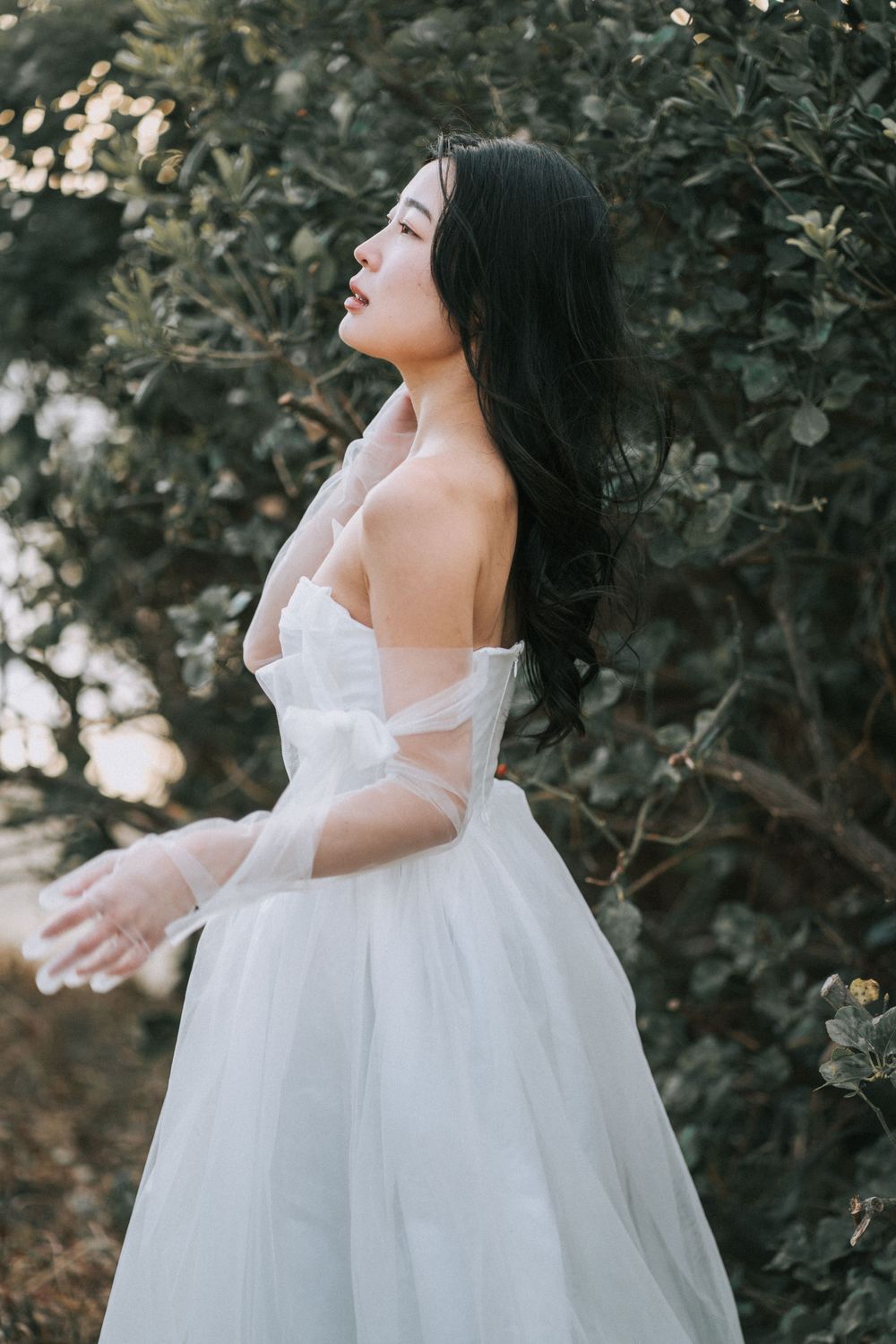 Beautiful Asian woman in a white wedding dress surrounded by the greenery of the PNW