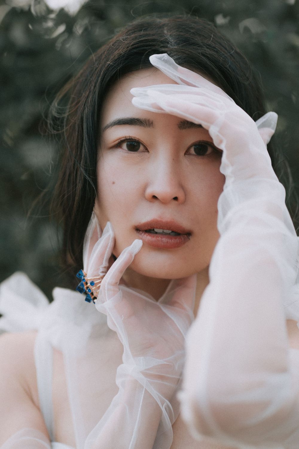 Female wearing a wedding dress and white tulle gloves, holding her hand up to frame her face