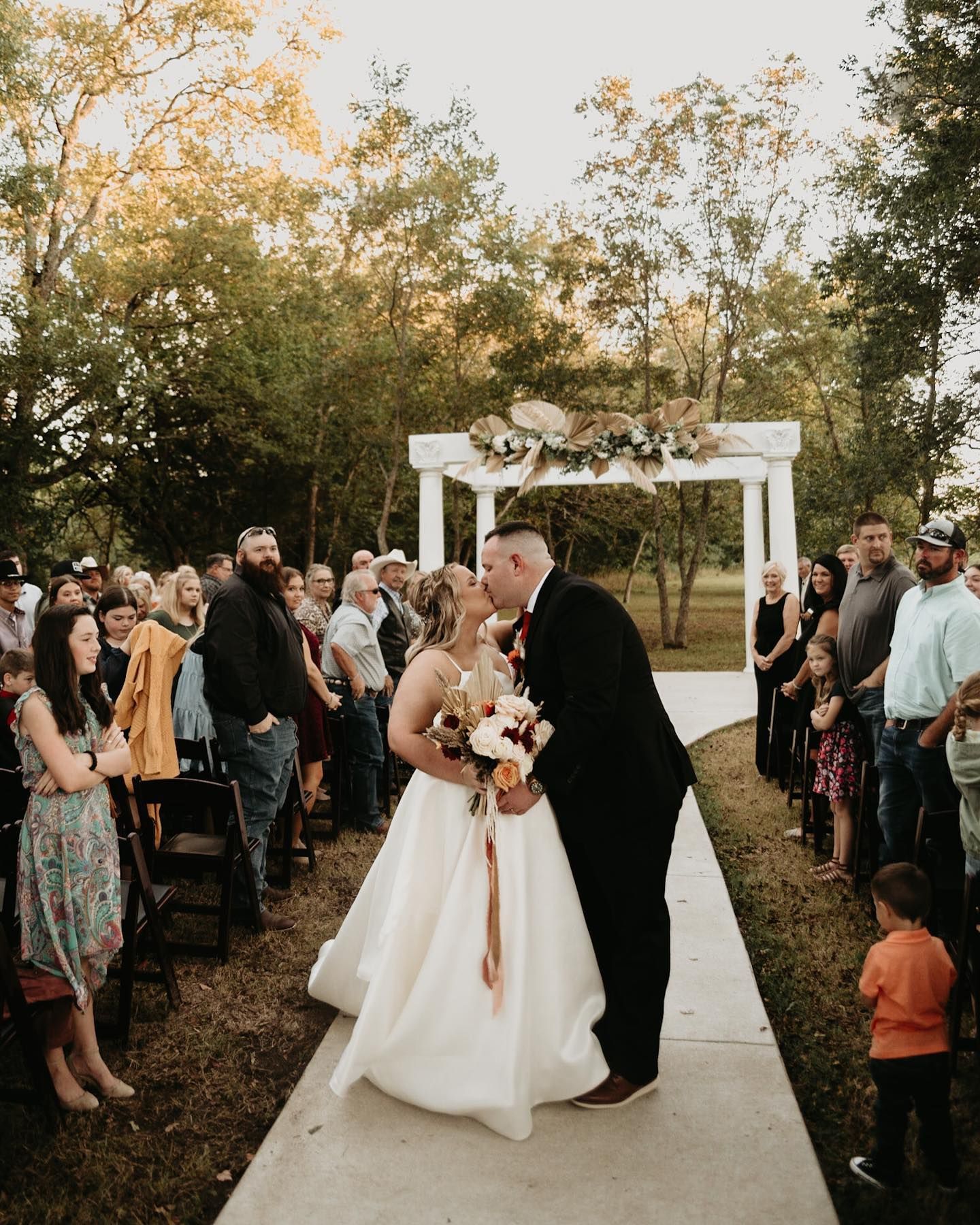Wedding ceremony under white arch with guests watching the celebration. Oklahoma Wedding Photographer