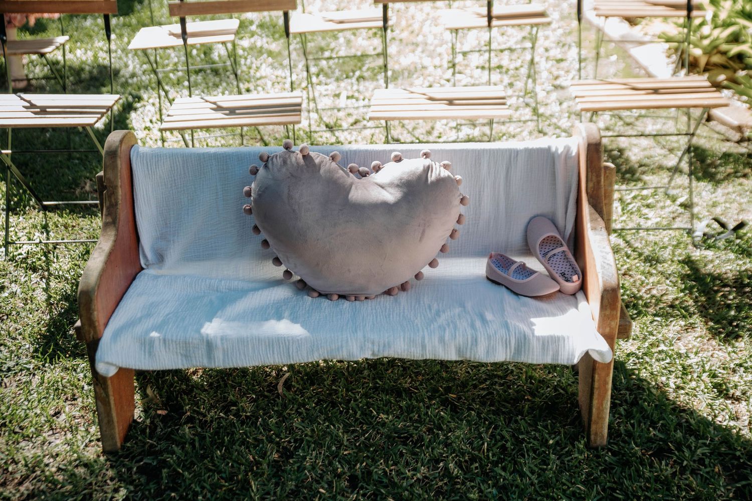 A rustic wooden bench with a heart-shaped pillow in a garden setting.