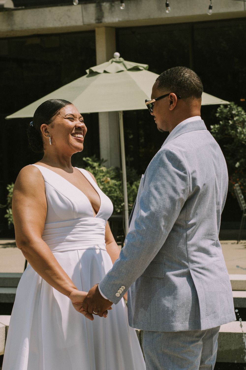 A newlywed couple holding hands and smiling outdoors on their wedding day, showcasing a wedding photoshoot.