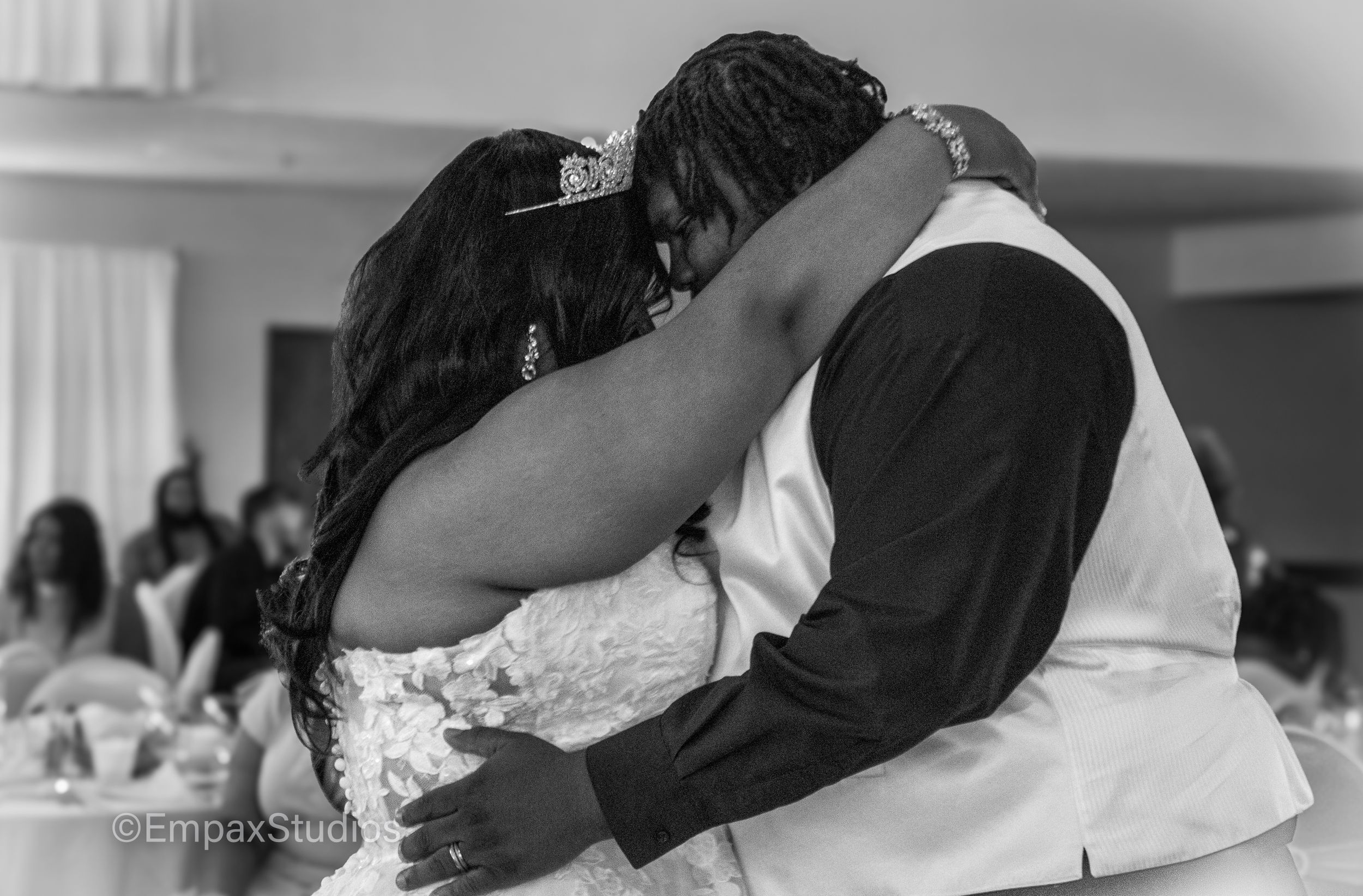 A black-and-white photo of a newlywed couple embracing during their first dance at the wedding reception.