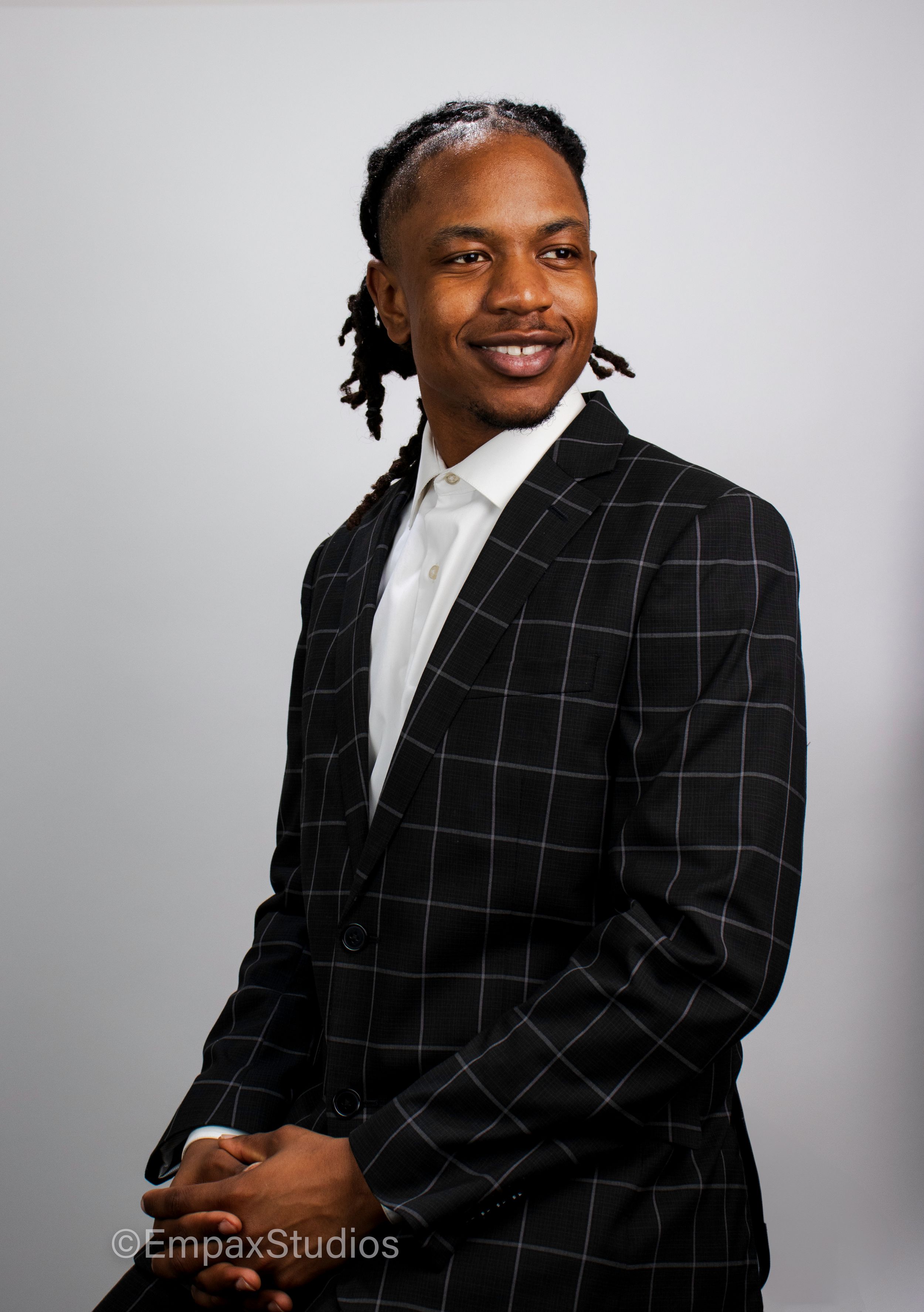 A confident black man in a black checkered suit poses against a neutral background, showcasing a professional portrait photography session.