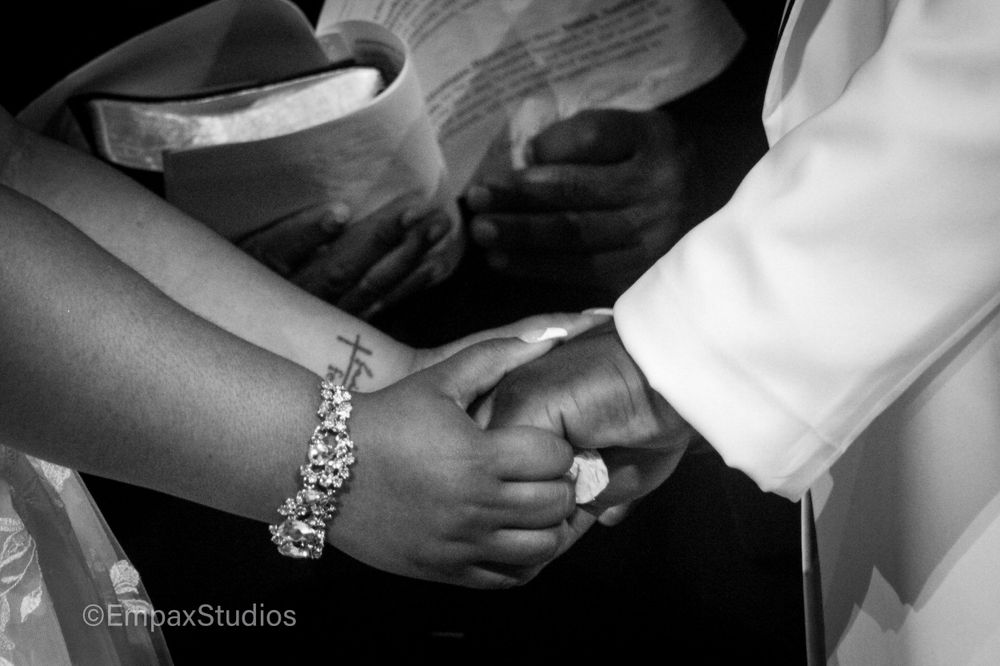 A black-and-white close-up of a newlywed couple holding hands during their wedding ceremony.