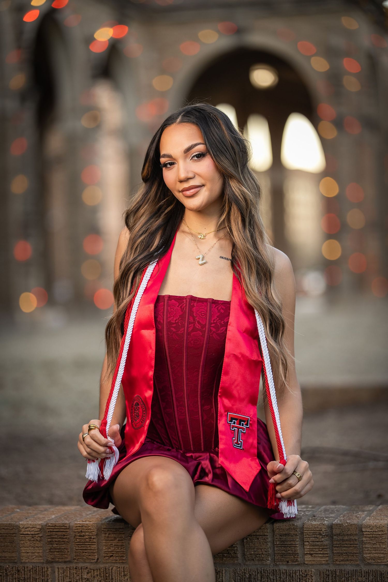 A person in a red velvet blazer poses against a blurred bokeh background during a graduation photo session.