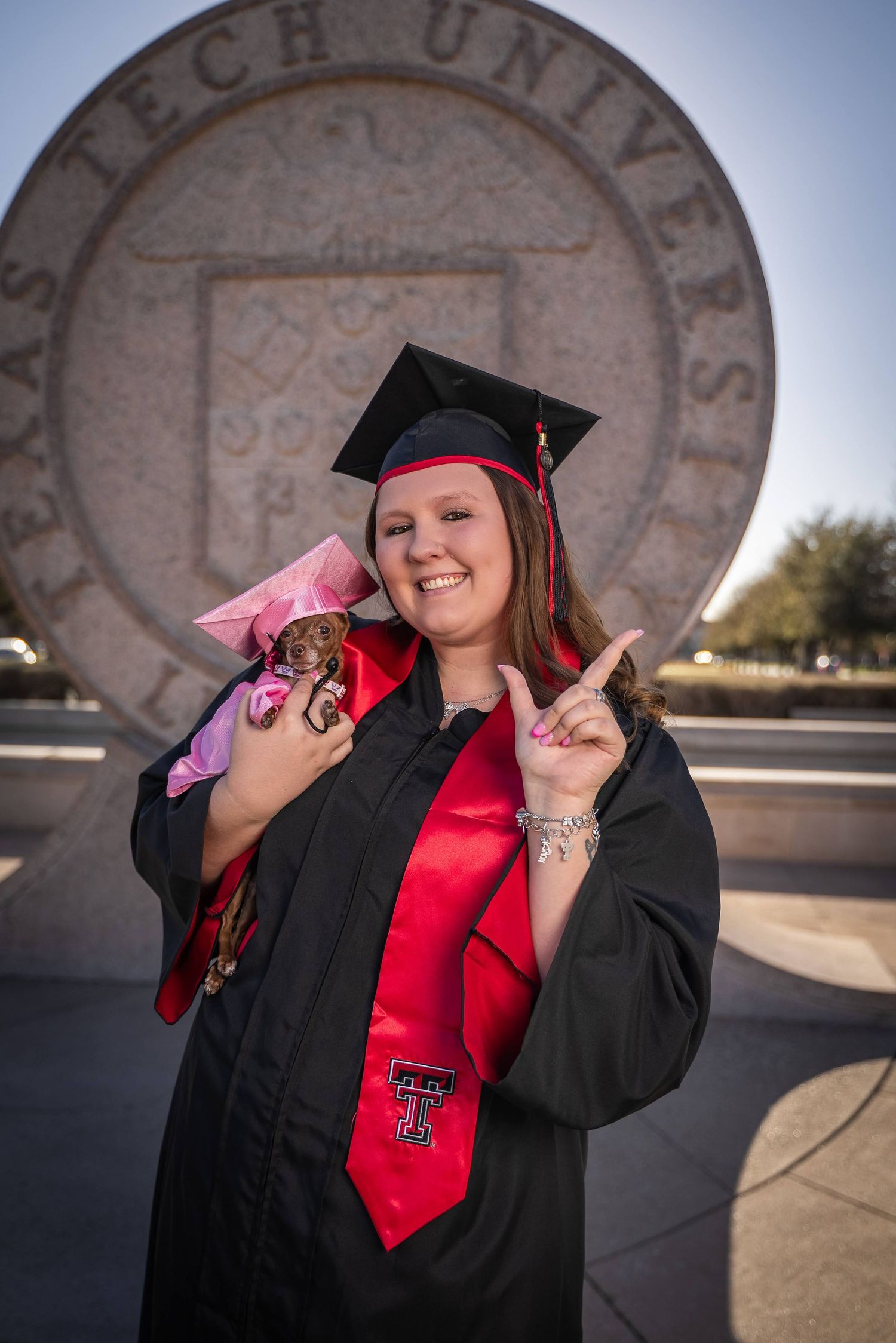 Graduate in red top and black cap and gown poses for graduation photos at Texas Tech University.