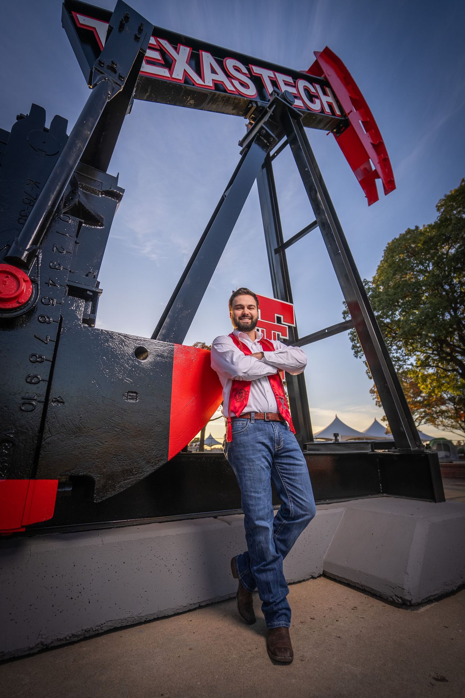 A person in overalls stands on an oil pump jack against a dramatic blue sky in Texas.