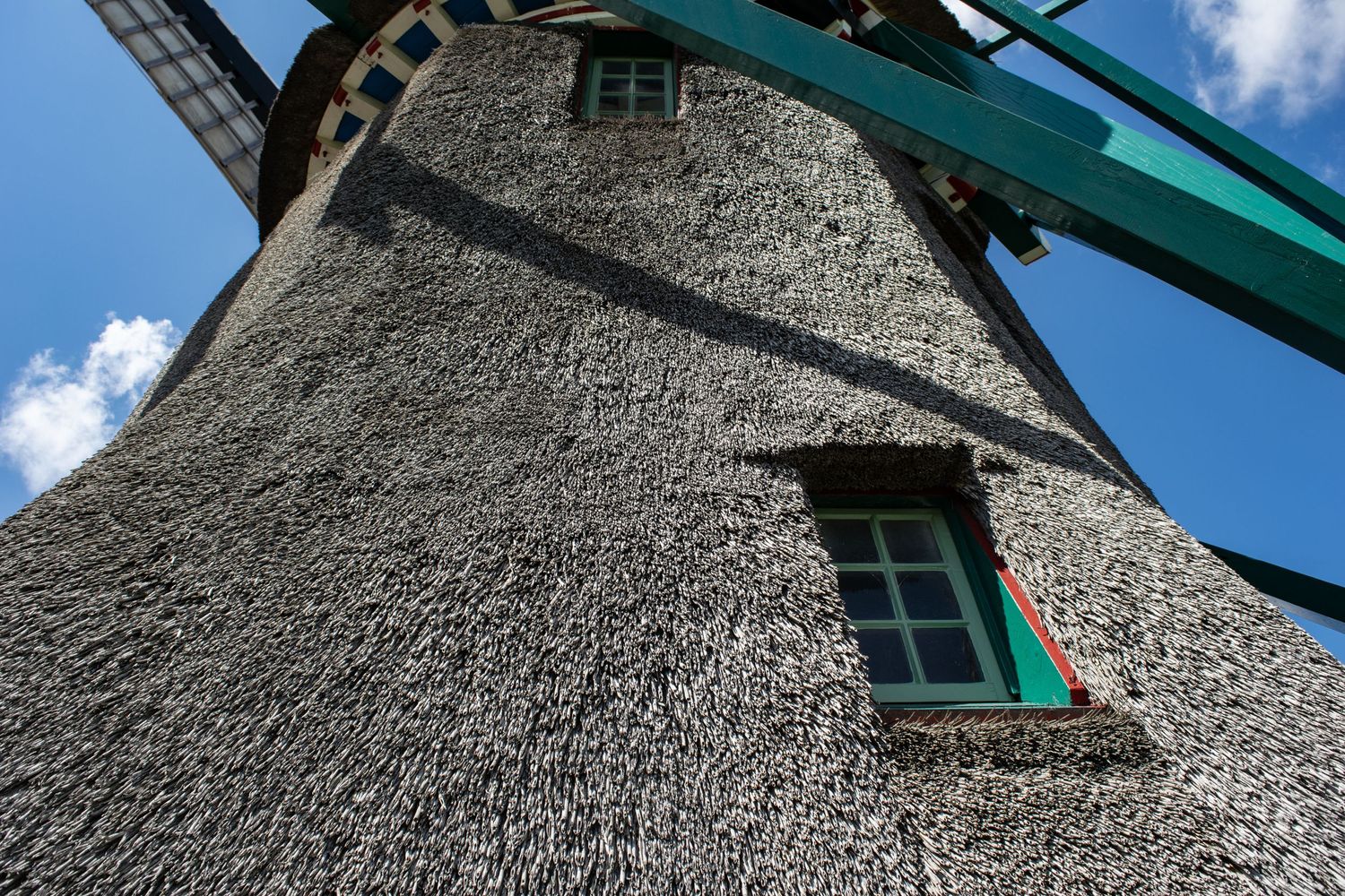 Close-up of a windmill's thatched roof exterior with green-trimmed window.