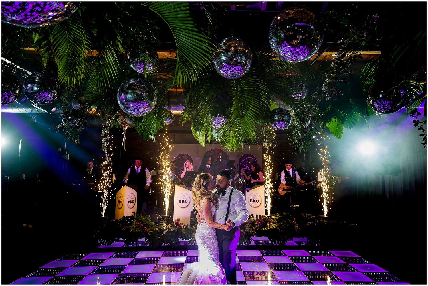 Nightclub style wedding reception with disco balls, palm trees and purple lighting effects.